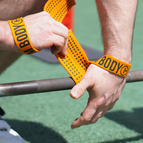 Man puts on Orange Weight Lifting Wrist Straps V1 to lift the barbell