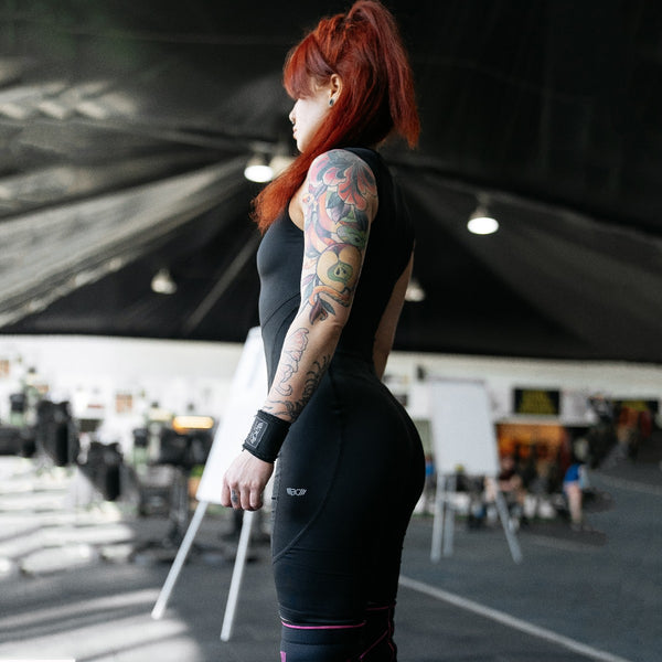 Person with tattoos wearing black WOMENS WEIGHTLIFTING COMPRESSION SINGLET S-3 with visible branding in an indoor setting (Side view) - Warm Body Cold Mind