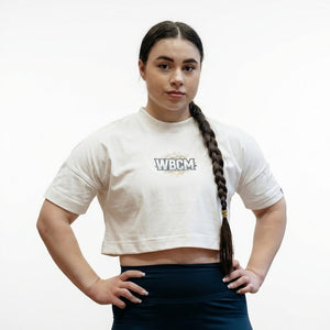 Person wearing a beige Women's Cropped T-shirt - Lift Off with 'WBCM' logo on a plain background - Warm Body Cold Mind